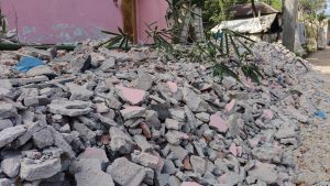 A pile of rubble consisting of broken concrete and bricks with scattered green bamboo leaves and a pink wall in the background.