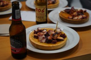 Two wooden trays of pulpo a feira sitting in a table with beer bottles