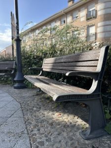 A wooden park bench with metal armrests and legs is situated on a pebble and stone walkway. 