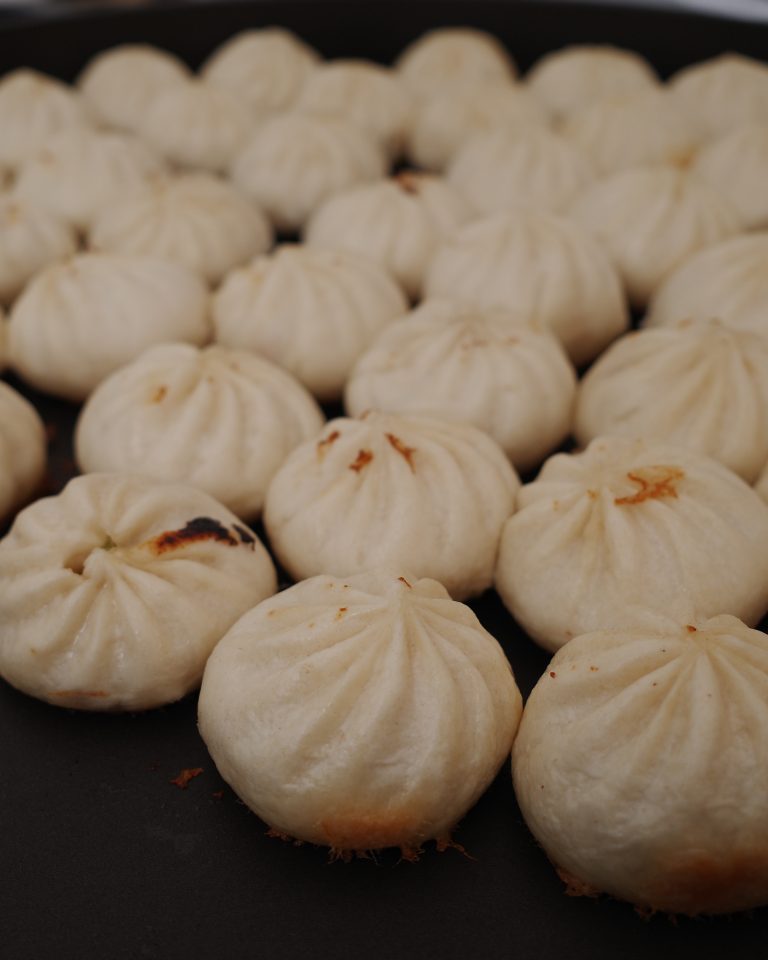 Mini siopao buns are being cooked on a nonstick griddle.