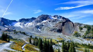 A mountainous landscape with rocky terrain and patches of snow near the peaks. A clear blue sky overhead with wispy clouds. Blackcomb, Whistler, BC - Canada