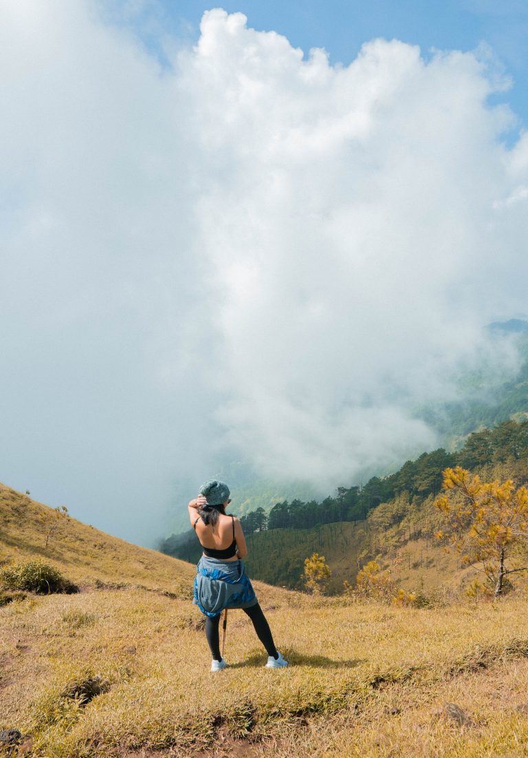 A woman stands on a mountain ridge at Mt. Ulap, gazing out over a vast sea of clouds that stretch across the horizon, surrounded by rugged peaks and lush greenery, capturing the serene beauty of nature.