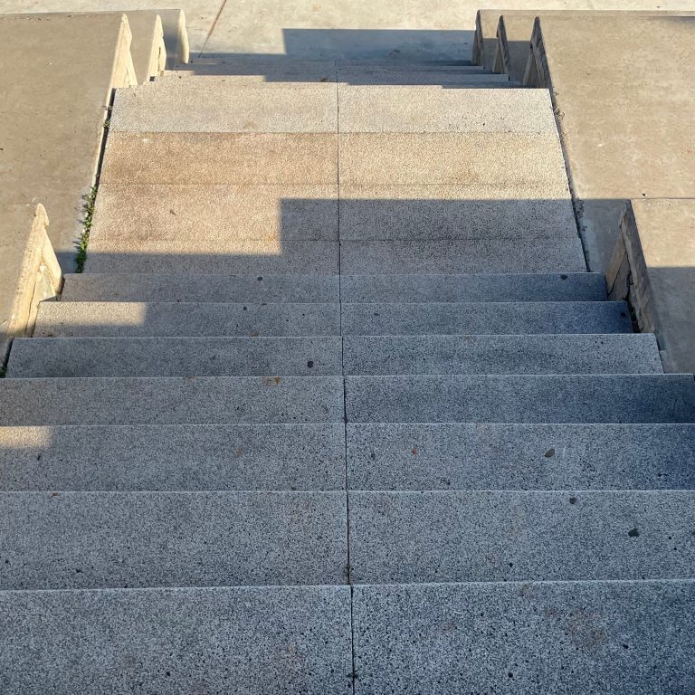 A gray concrete stair tread with a simple, rustic design. The steps have slightly irregular edges, reflecting a less polished finish. The concrete shows natural textures and subtle variations in color, highlighting its robust and functional character.