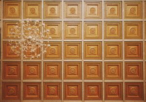 A grand, ornate ceiling with embossed textures and a sparkling chandelier, viewed from below.