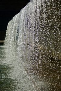 View larger photo: Close-up view of water cascading down a textured wall, creating a shimmering and sparkling effect as the sunlight hits the droplets.