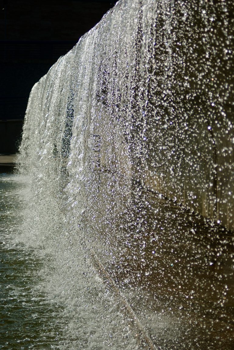 Close-up view of water cascading down a textured wall, creating a shimmering and sparkling effect as the sunlight hits the droplets.