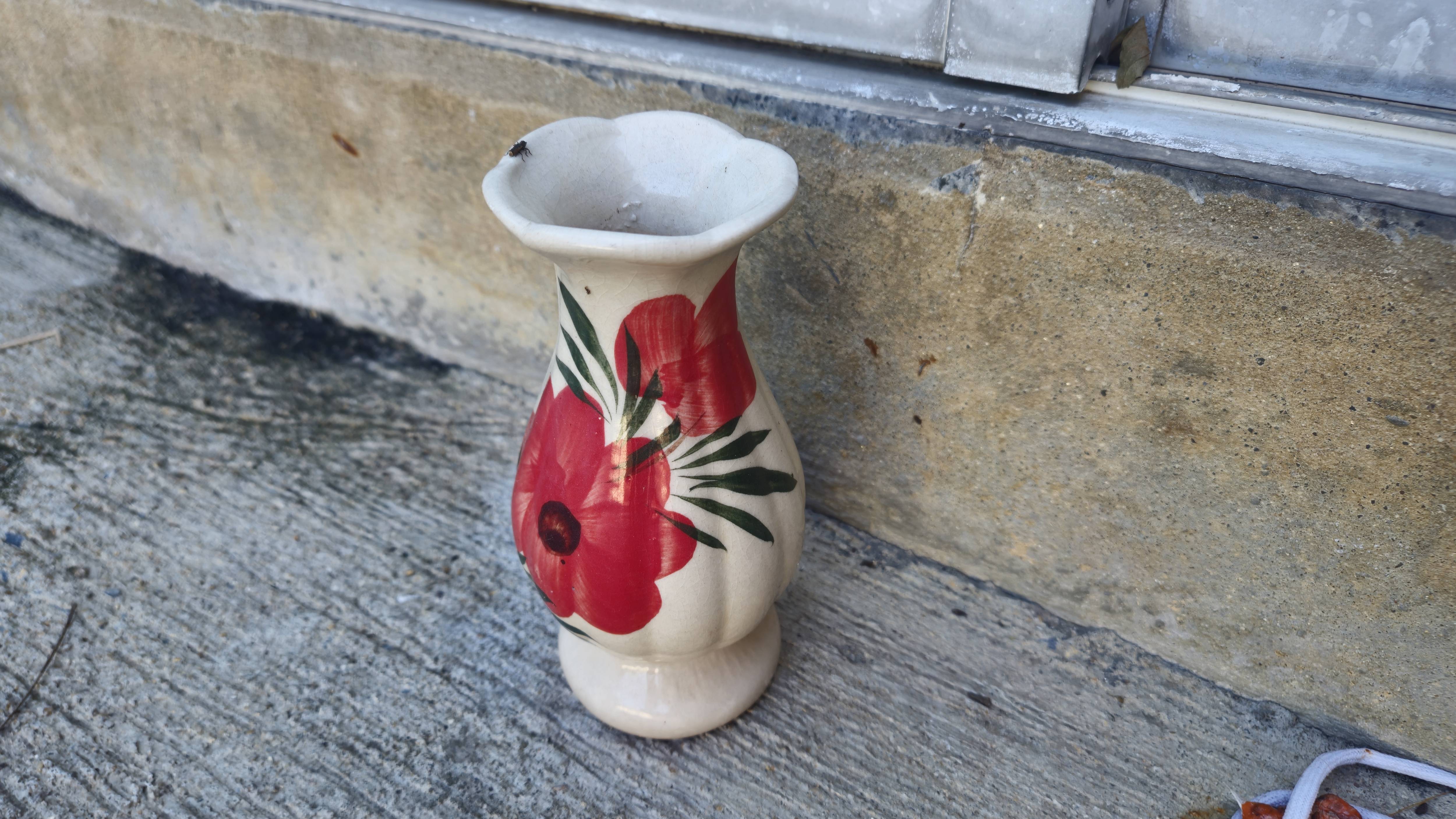 A ceramic vase with a wide top, painted with a design of red flowers and green leaves.