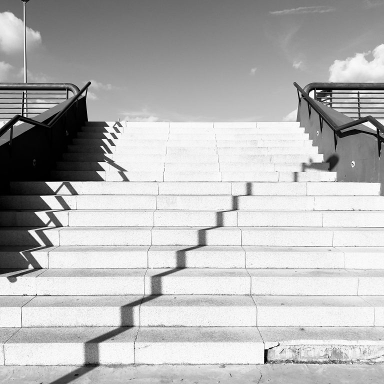 Black and white image. Concrete stairs with metal railings made of tubes. View from the lower level.