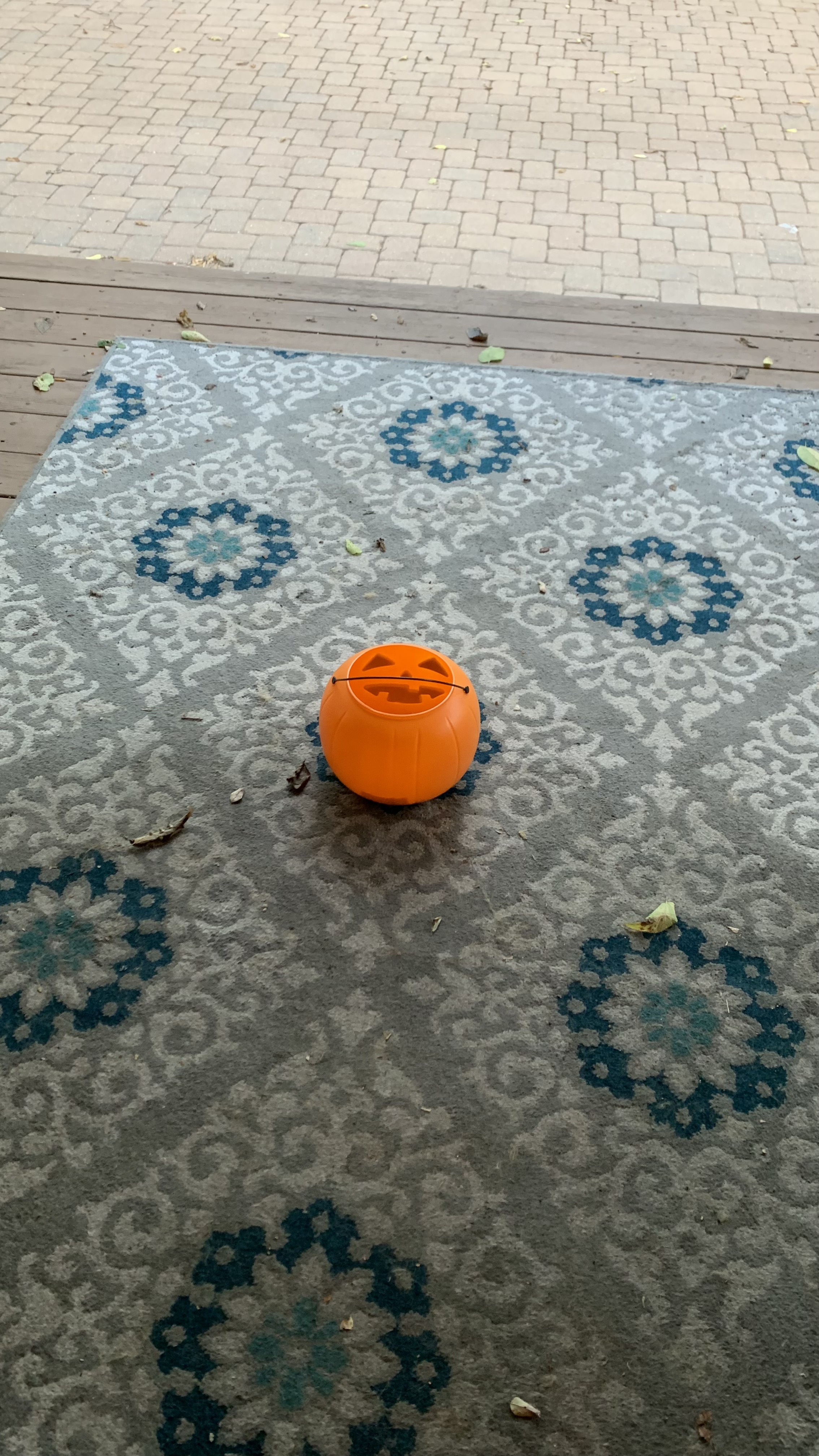 Empty jack-o-lantern basket sitting on top of a rug on a wood porch with a paver brick walkway in the background