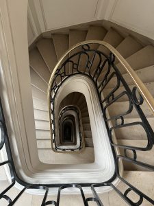 A spiraling staircase viewed from above, showcasing ornate metal railings and descending steps that form a geometric pattern.