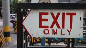 an Exit Only sign written with red letters on a white background with directional arrows pointing left