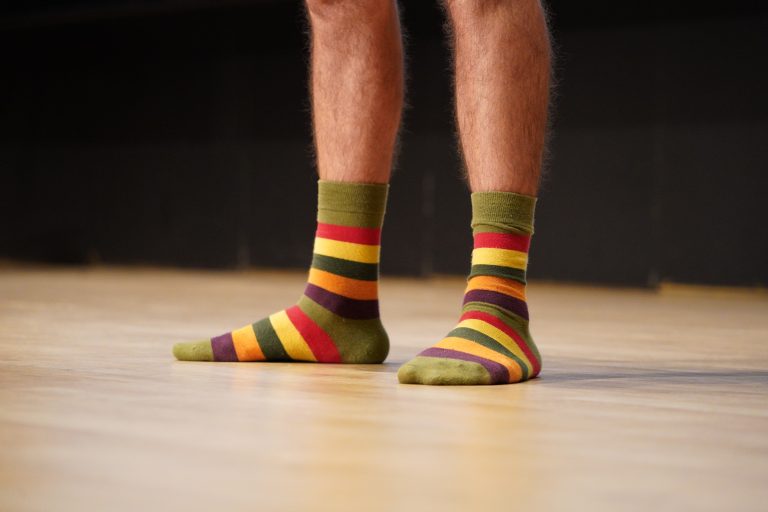 A person’s legs wearing colorful striped socks, standing on the wooden floor of a stage.