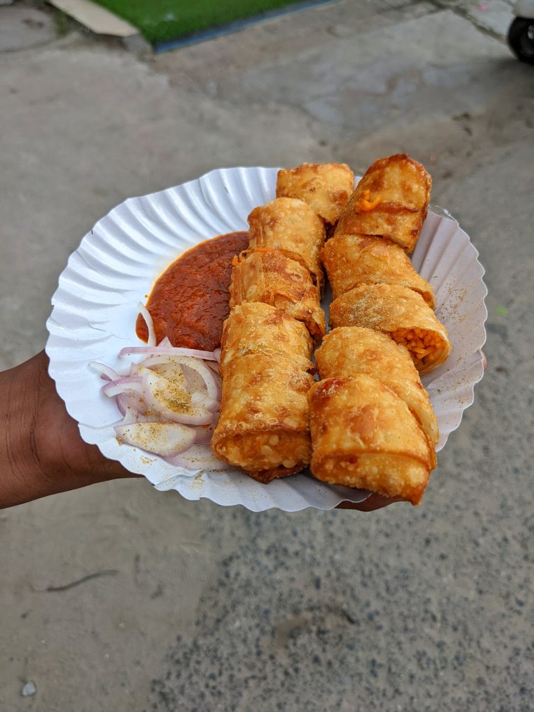 Food spring roll in a plate with red spice sauce with onion.