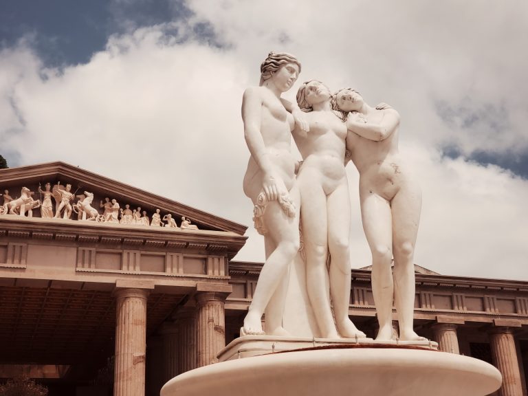 A sculpture of three women embracing in the foreground, with the majestic Temple of Leah in the background.