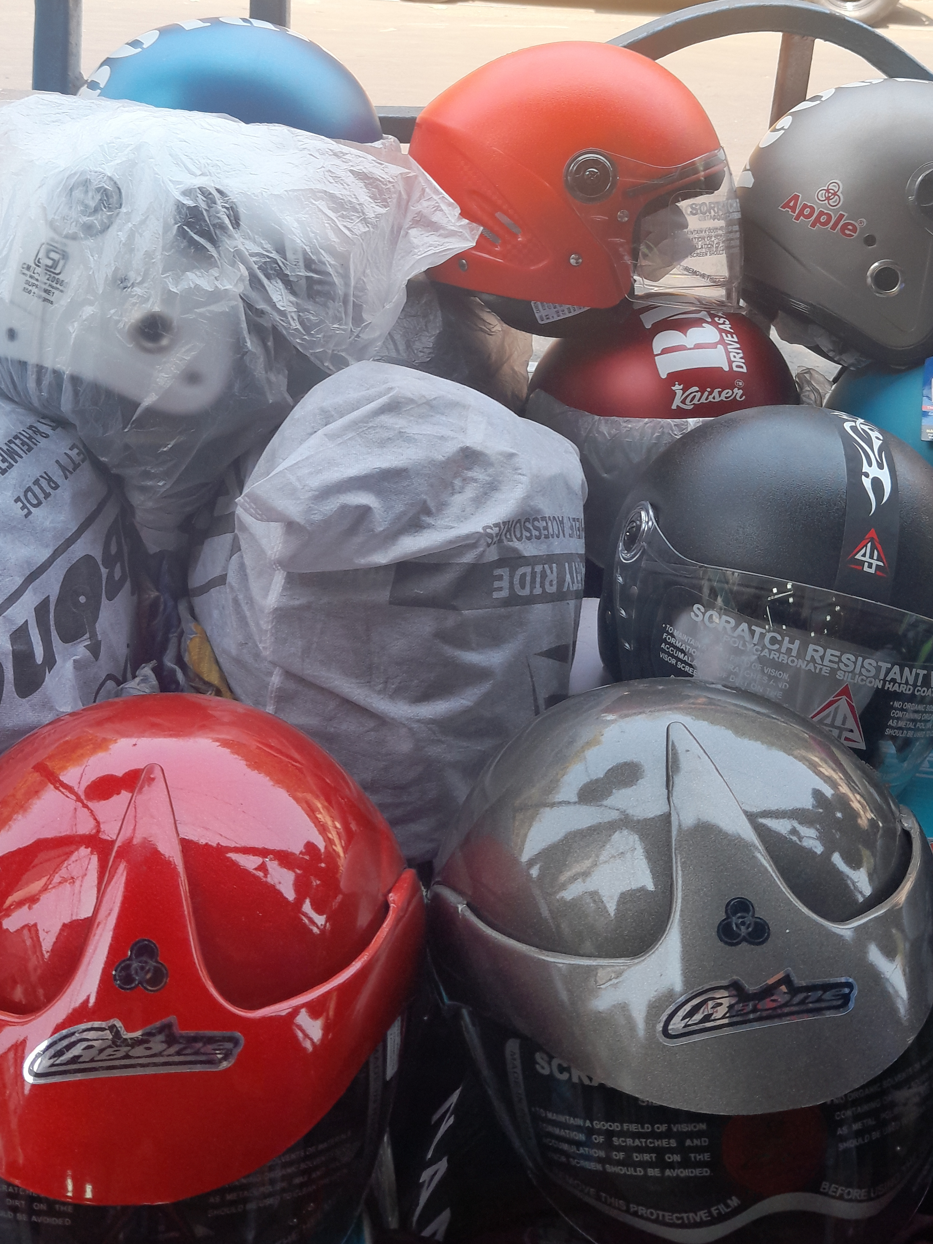 A collection of various motorcycle helmets, including red, blue, silver, and black models, some wrapped in protective plastic.