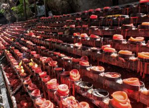 A collection of red votive candles, some still lit and others melted, arranged in a line.