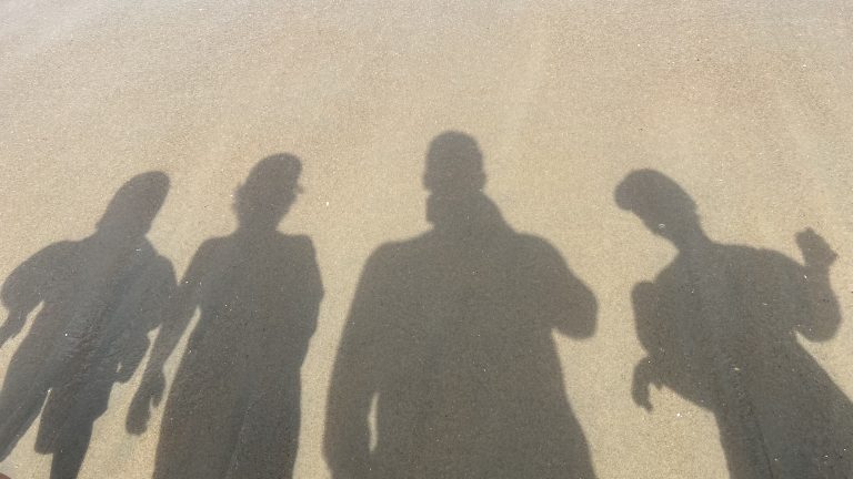 Silhouettes of four people laid out on a sandy beach