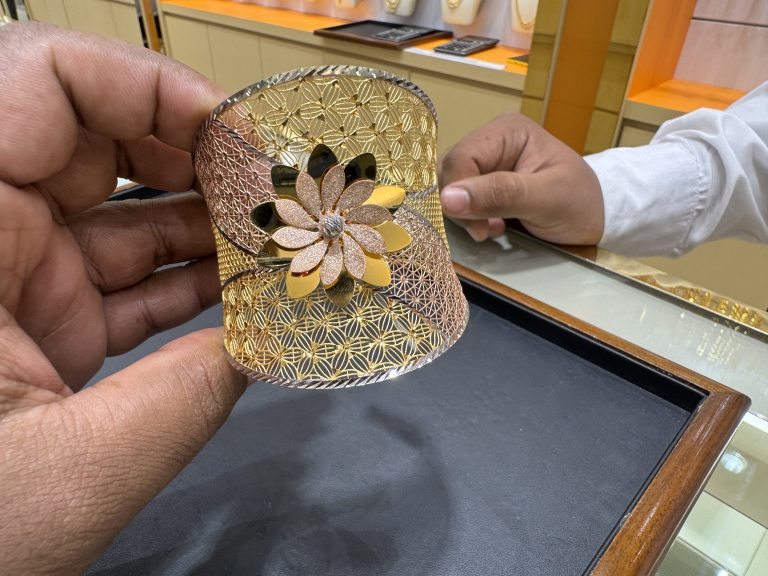 Intricate gold bracelet with a floral design, held by two people in a jewelry store.