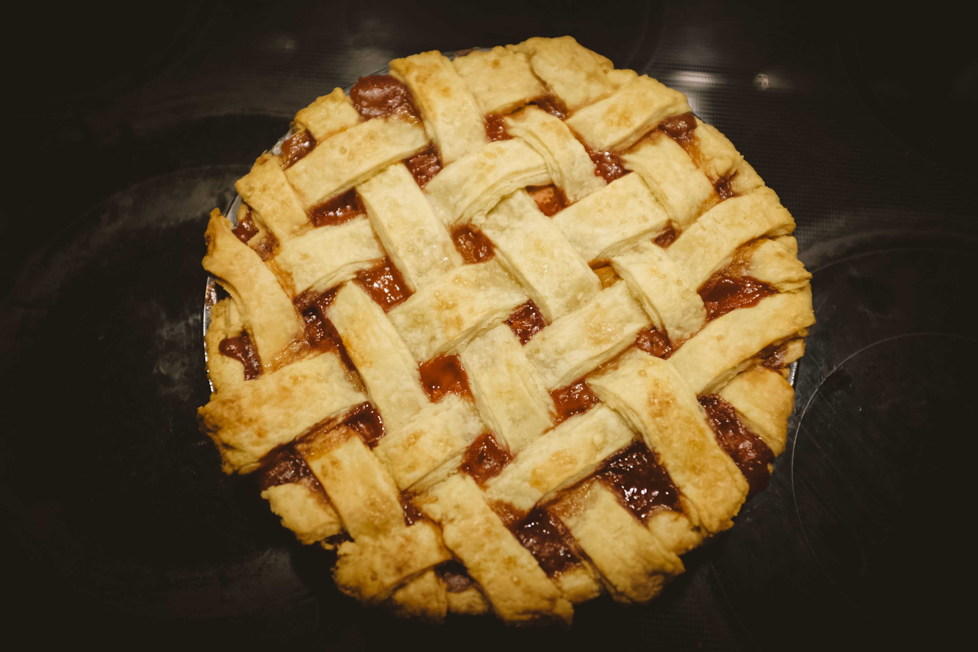 View from above of a peach and strawberry pie, fresh out of the open, on a black stove top.