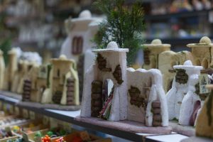 A display of miniature clay houses resembling traditional architecture, with detailed textures and small trees. They are arranged on shelves with various colors and designs.