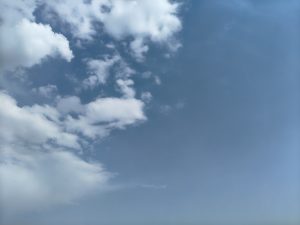 A clear blue sky with scattered fluffy white clouds.