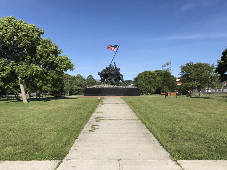 A long sidewalk leading to a World War II monument in Bicentennial Park in Fall River, Massachusetts depicting soldiers raising the US flag during the Battle of Iwo JIma.