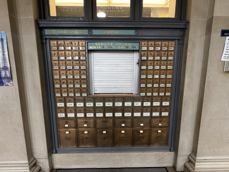 A set of old, metal Post Office boxes for the  New Bedford, Massachusetts post office at zip code 02742. There is a small, closed service window in the middle, and the boxes are 4 different sizes.