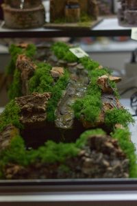 A decorative display featuring a miniature landscape with artificial moss, small rocks, and a water feature resembling a stream.