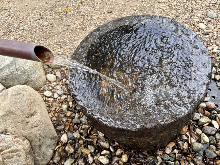 A copper spout pours water into an overflowing stone bowl.