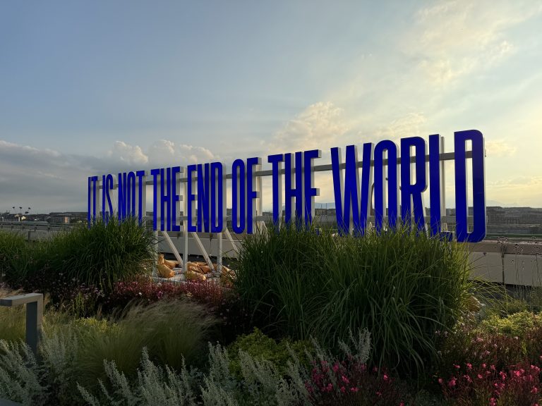 A large sign behind a garden reading “it is not the end of the world” in blue letters at the top of the lingotto building in torino, italy.