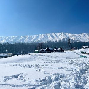 A snow-covered valley surrounded by pine forests and mountains, with a small wooden house in the landscape.