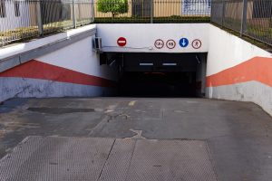 Entrance to an underground parking garage with a sloped ramp. The walls have red and white diagonal stripes, and there are several traffic signs.
