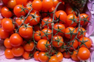 A close-up image of vibrant red cherry tomatoes still attached to their green stems, arranged on a purple surface.