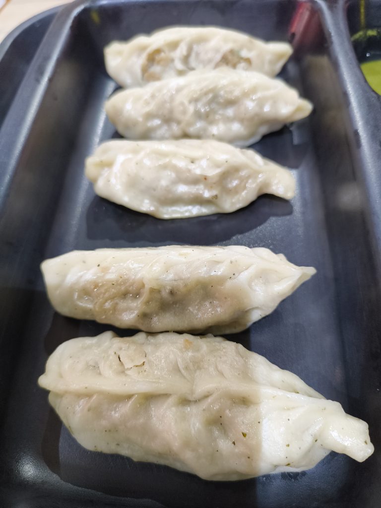 Five steamed dumplings arranged in a row on a dark, rectangular tray.