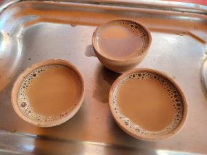 Three clay cups filled with tea on a metallic tray.