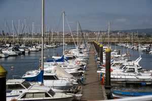 A busy marina filled with numerous sailboats and yachts docked along both sides of a wooden pier extending into the water.