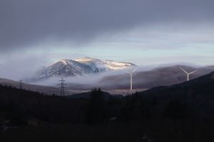 Wind turbines, standing in a misty, mountainous landscape in the Scottish Highlands