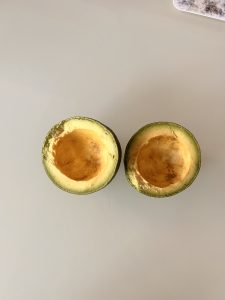 Two ripe avocado halves with the pit removed, placed on a light gray surface.