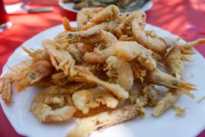 A plate of fried shrimp, served on a white dish with a red tablecloth in the background.