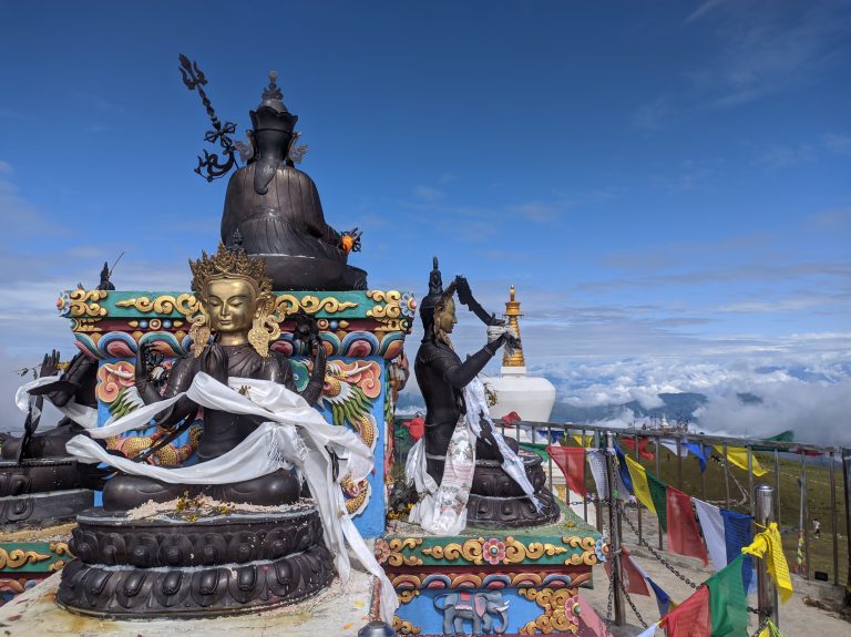 A richly decorated Buddhist statue sits atop a colorful, ornate pedestal adorned with traditional Tibetan motifs.