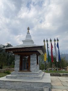 A small temple in the courtyard with prayer flags in the background.