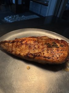 A grilled piece of meat on a metal plate, with visible char marks and herbs on top.