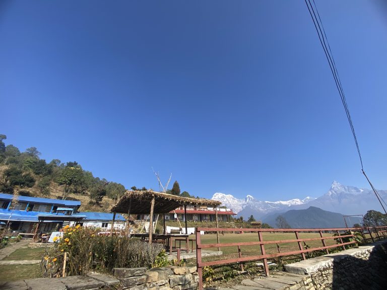 Australian base camp.A snow-capped mountain range is visible in the background. In the foreground, there are stone paths, wooden railings, and flowering plants.