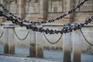 Close-up of metal chains suspended between stone pillars with a blurred stone building in the background.