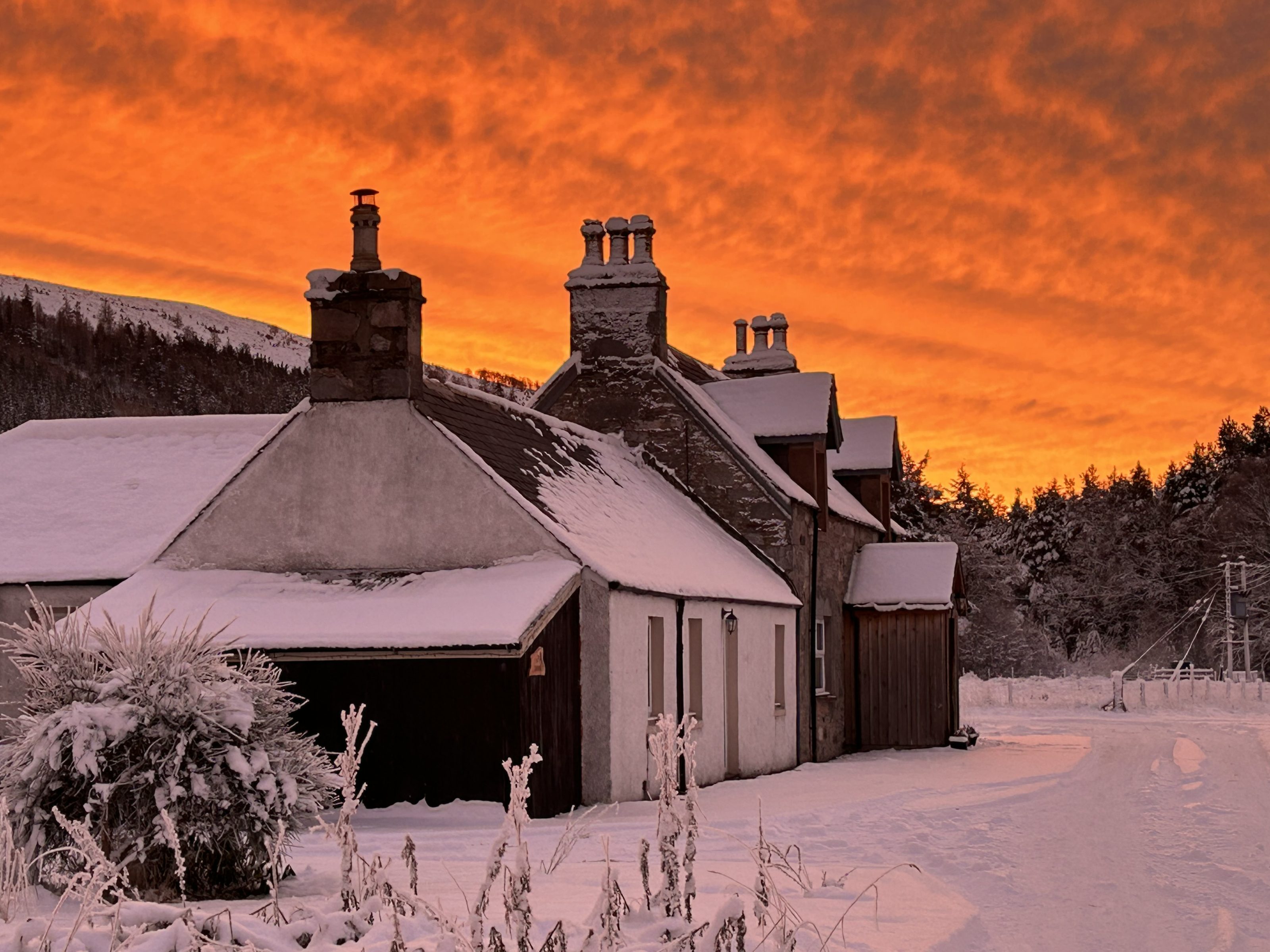 Two old semi detached cottages in the Scottish Highlands at sunrise. Sky is vivid orange the entire scene snow covered.