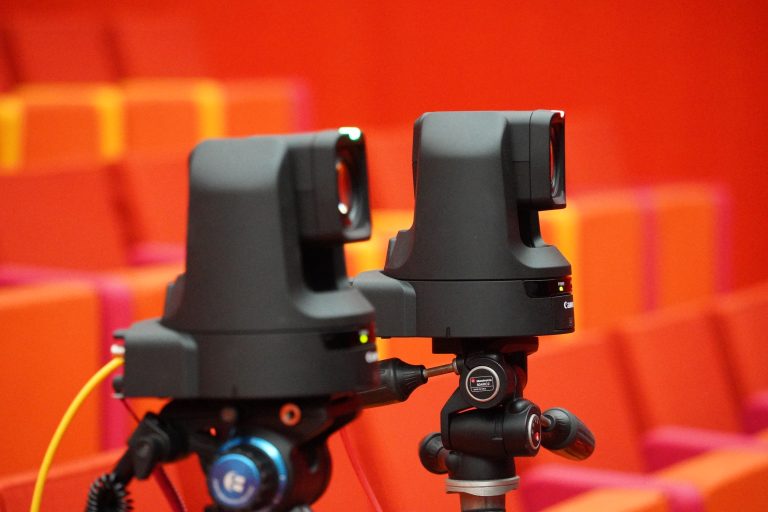 Two black PTZ cameras mounted on tripods with a blurred vibrant orange and red background.