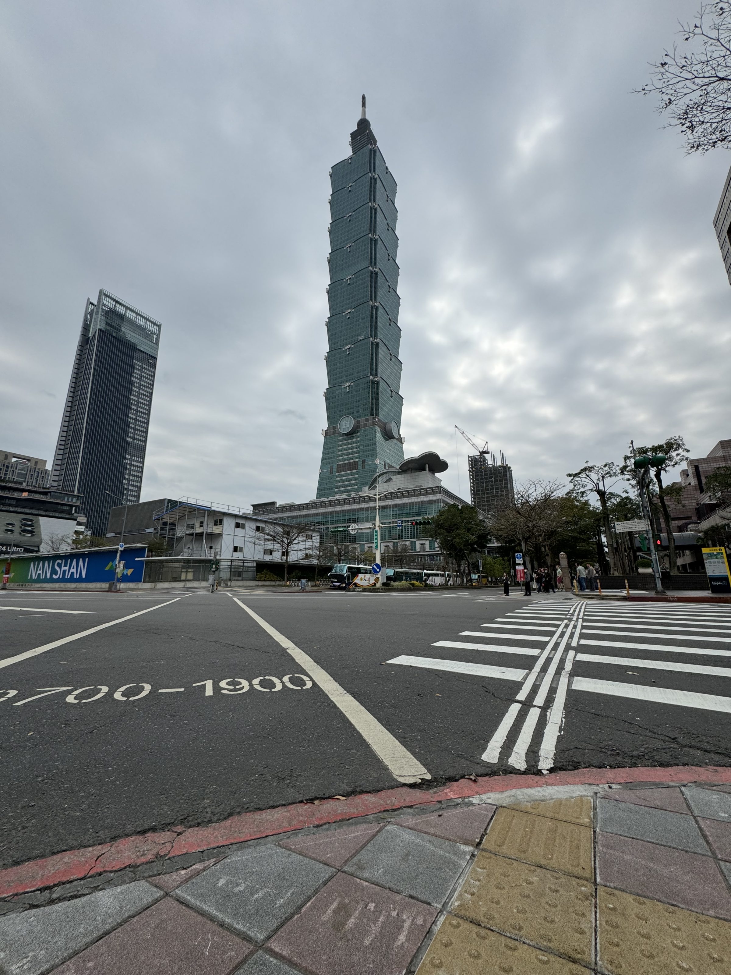 A large intersection in Taipei, Taiwan. The Taipei 101 building and a group of people waiting to cross the street are visible in the background.
