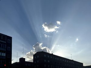 Sunbeams rising behind a building and clouds with blue sky