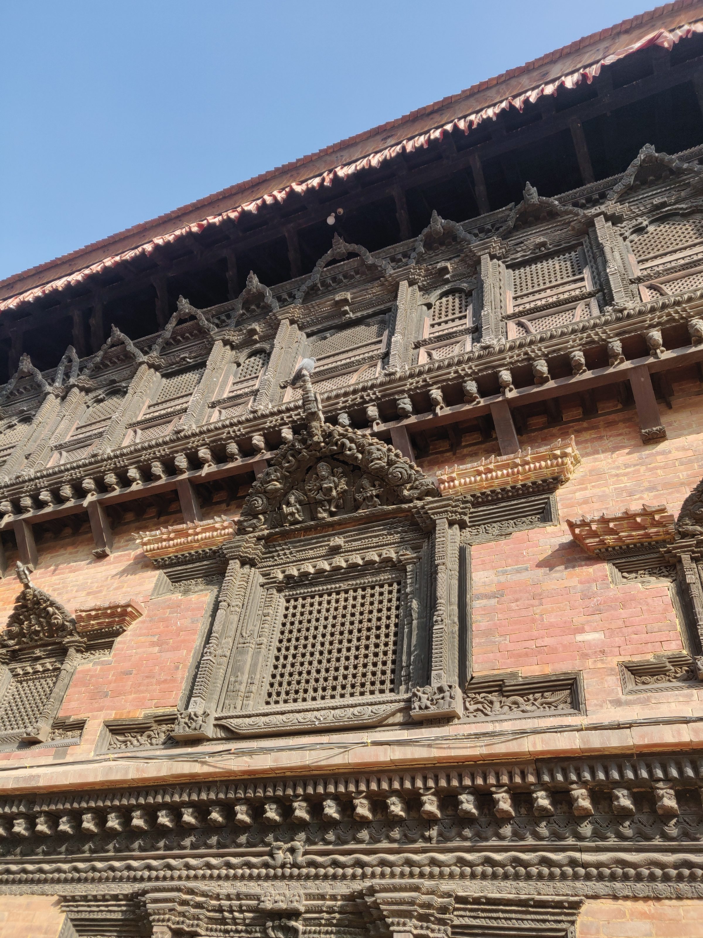 Ornate architectural detailing on a historic brick building, featuring intricate wood carvings and decorative patterns around windows, set against a clear blue sky.