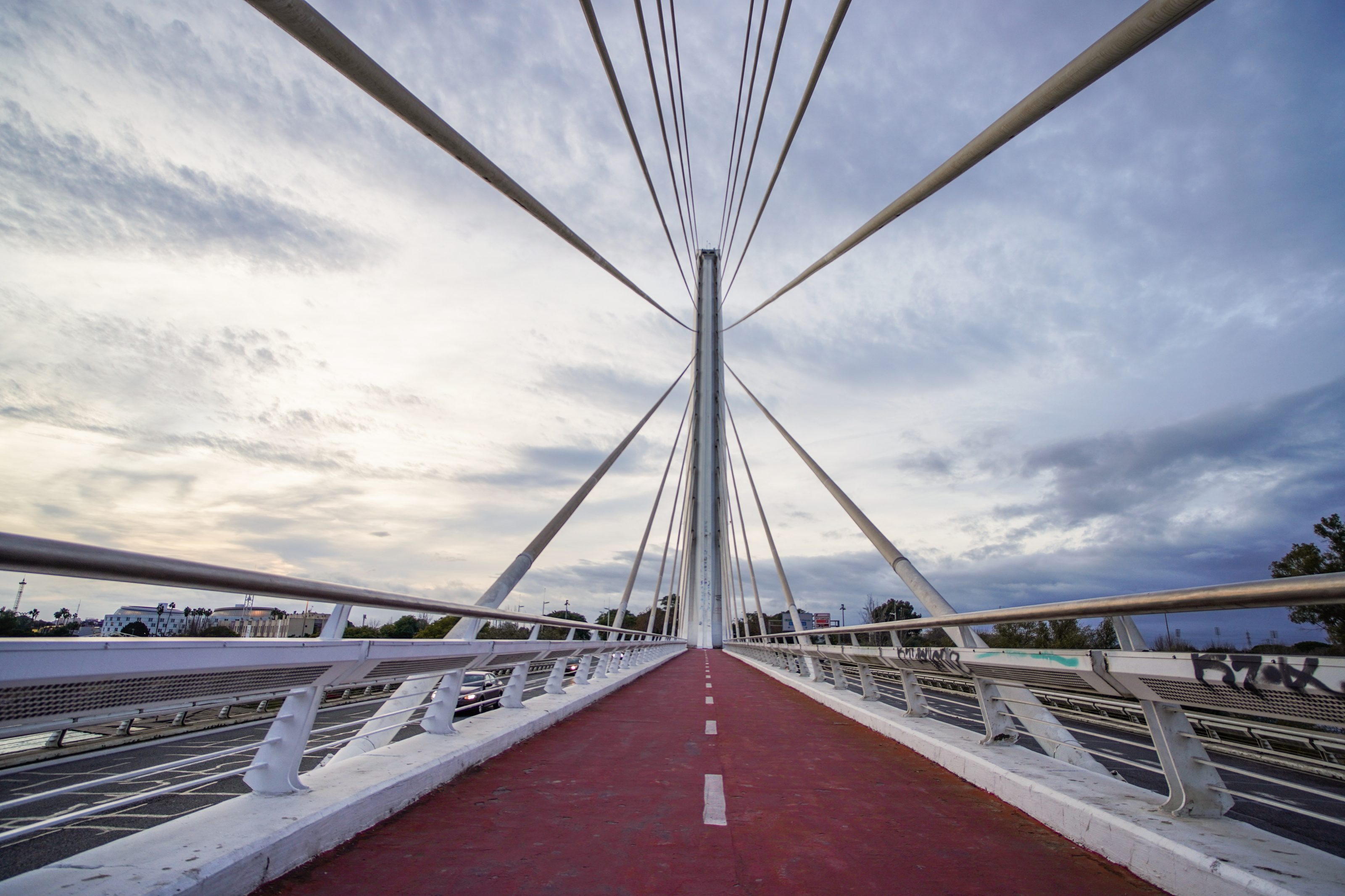 Puente del Alamillo, Sevilla. A modern cable-stayed bridge with a red pedestrian path running down the center. The bridge is framed by cables extending from the central tower to the edges.